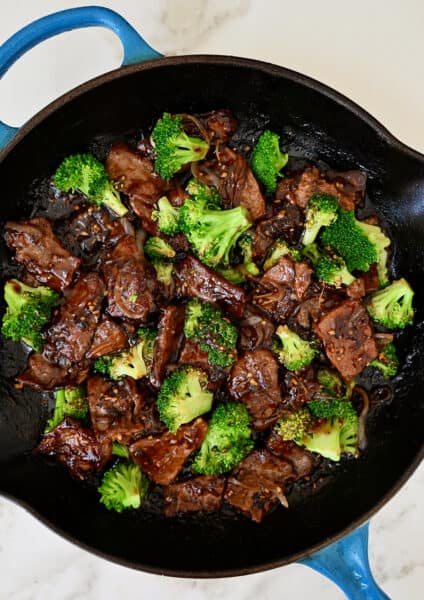 A large skillet containing beef and broccoli coated in a garlicky soy sauce.