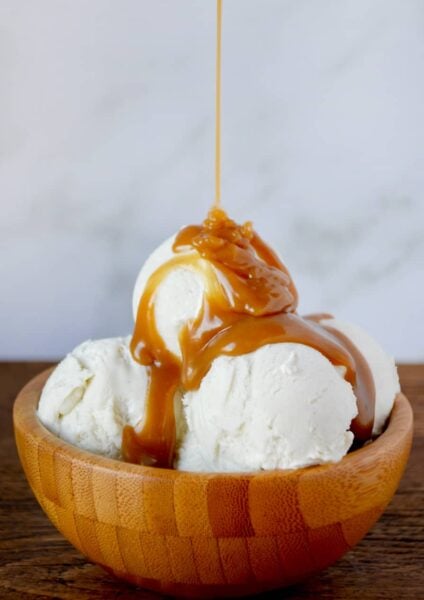 Easy Homemade Butterscotch Sauce poured over vanilla ice cream in wooden bowl