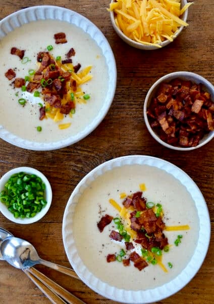 Two bowls containing creamy potato soup topped with crispy bacon, shredded cheddar cheese, a dollop of sour cream and sliced green onions.