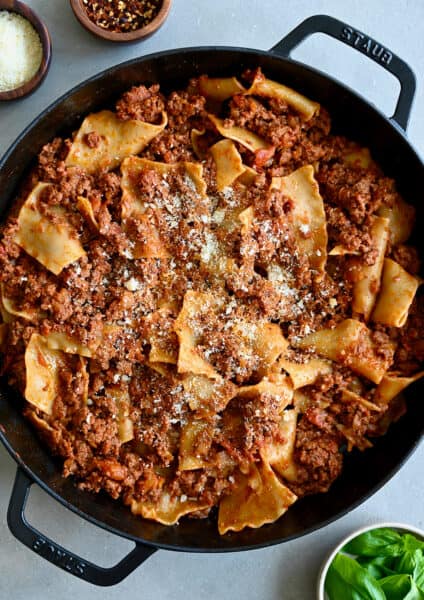 A cast iron skillet containing hearty beef lasagna garnished with grated Parmesan cheese.
