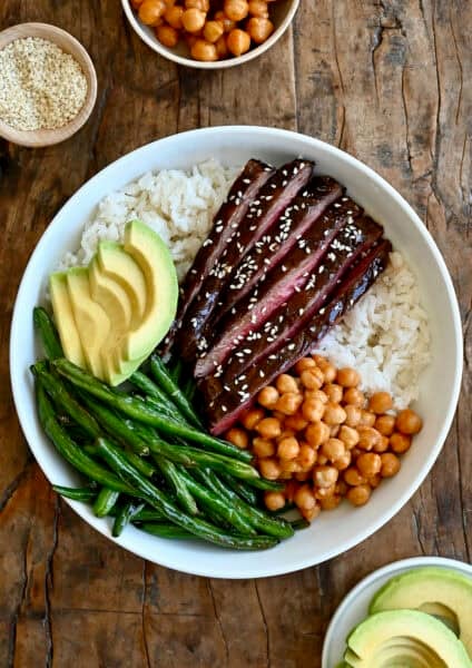 Beef teriyaki bowl with thin slices of steak, coconut rice, Chinese green beans, avocado and chickpeas tossed in peanut sauce.