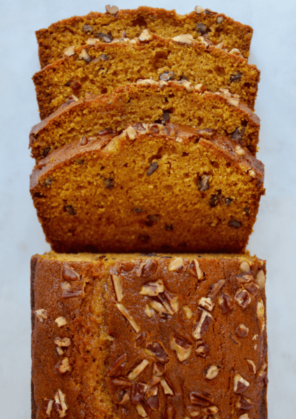 A loaf of pumpkin bread topped with pecans with four pieces sliced off of it.